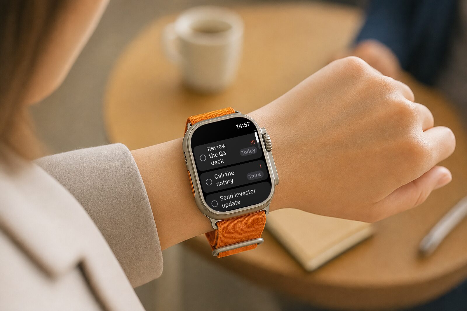 עמוד המשימות ב-Routines ל-Apple Watch: שורות שכתוב בהן Review the Q3 deck עם שלושה סימני קריאה ותווית Today, ‏Call the notary עם סימן קריאה אחד ותווית Tmrw, ו-Send investor update, ולכל אחת עיגול סימון שנוגעים בו, על Apple Watch Ultra על פרק ידה של אישה מעל שולחן קפה.